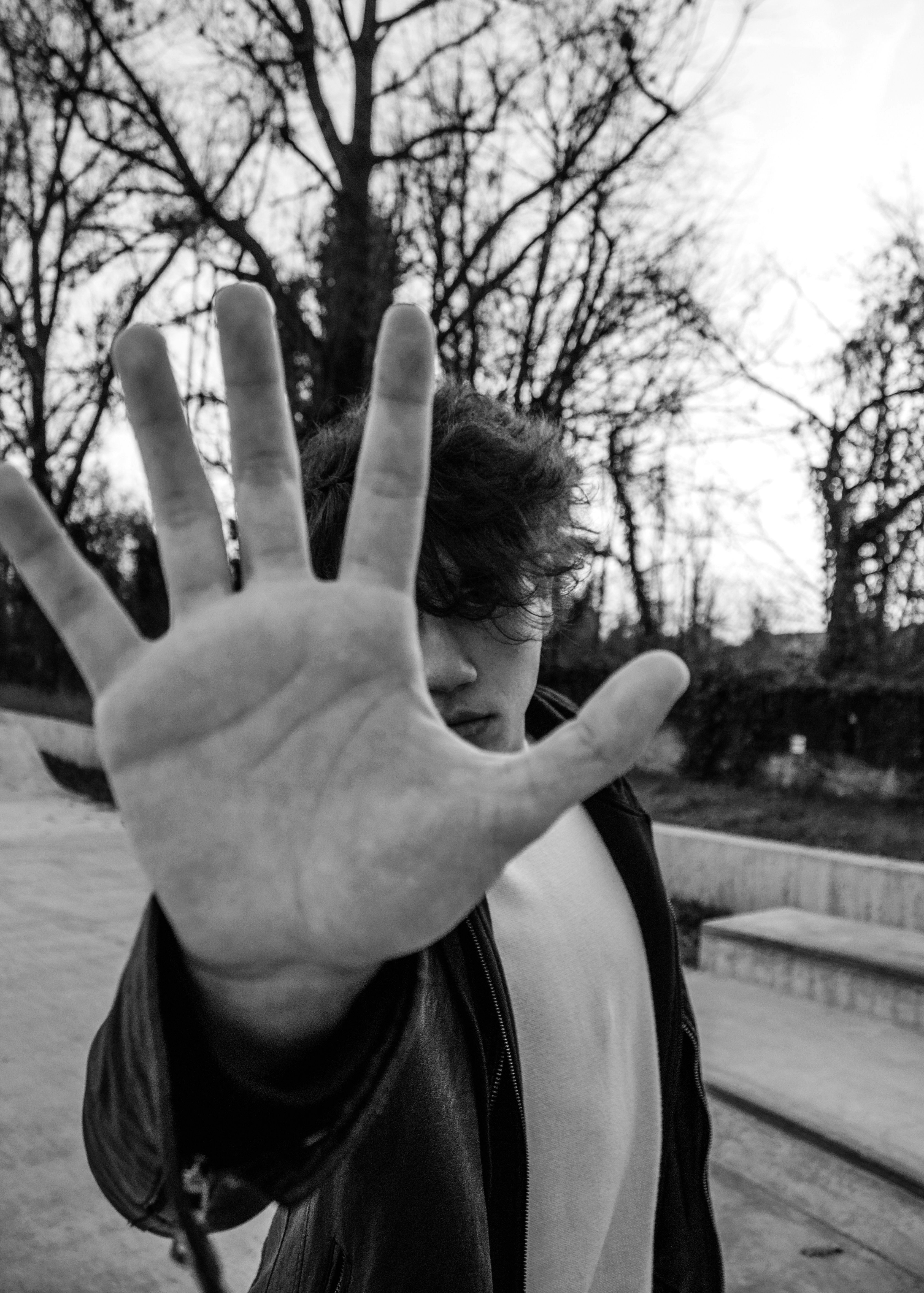 A young man holds his palm up directly at the camera, face obscured, in a clear gesture of refusal.